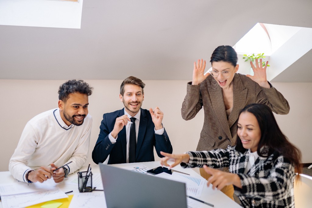Begeistertes Team feiert gemeinsam einen Erfolg vor dem Laptop im Büro